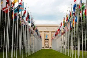 From below of various flags on flagpoles located in green park in front of entrance to the UN headquarters in Geneva where Avi Perera attended the inaugural UN conference on AI, Security, and Ethics