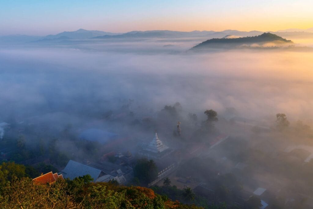 Serene landscape of Northern Thailand with mountains rising above a sea of mist at sunrise, representing the peace and nature of the country.